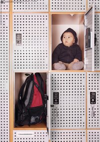 Ein Foto von mehreren Schließfächern, wahrscheinlich in einer Bibliothek. In einem der zwei geöffneten Schließfächer ist ein Rucksack zu sehen, in dem anderen - ein verwundert schauendes Baby in einem Kaputzenpulli.